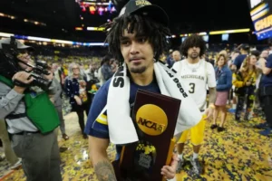 Michigan Wolverines player holds NCAA championship trophy on confetti-covered court after defeating UConn in the 2026 national title game