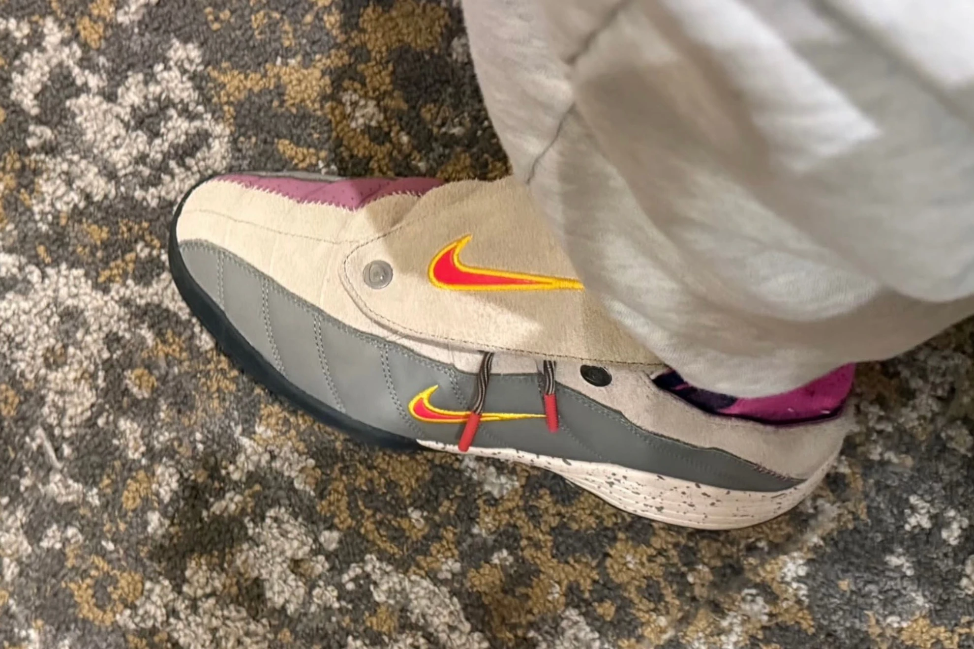 On-foot view of the Nike Total 90 Mule by Kids of Immigrants featuring khaki suede upper, grey leather panels, and red-yellow Swoosh with snap-button fold-over tongue