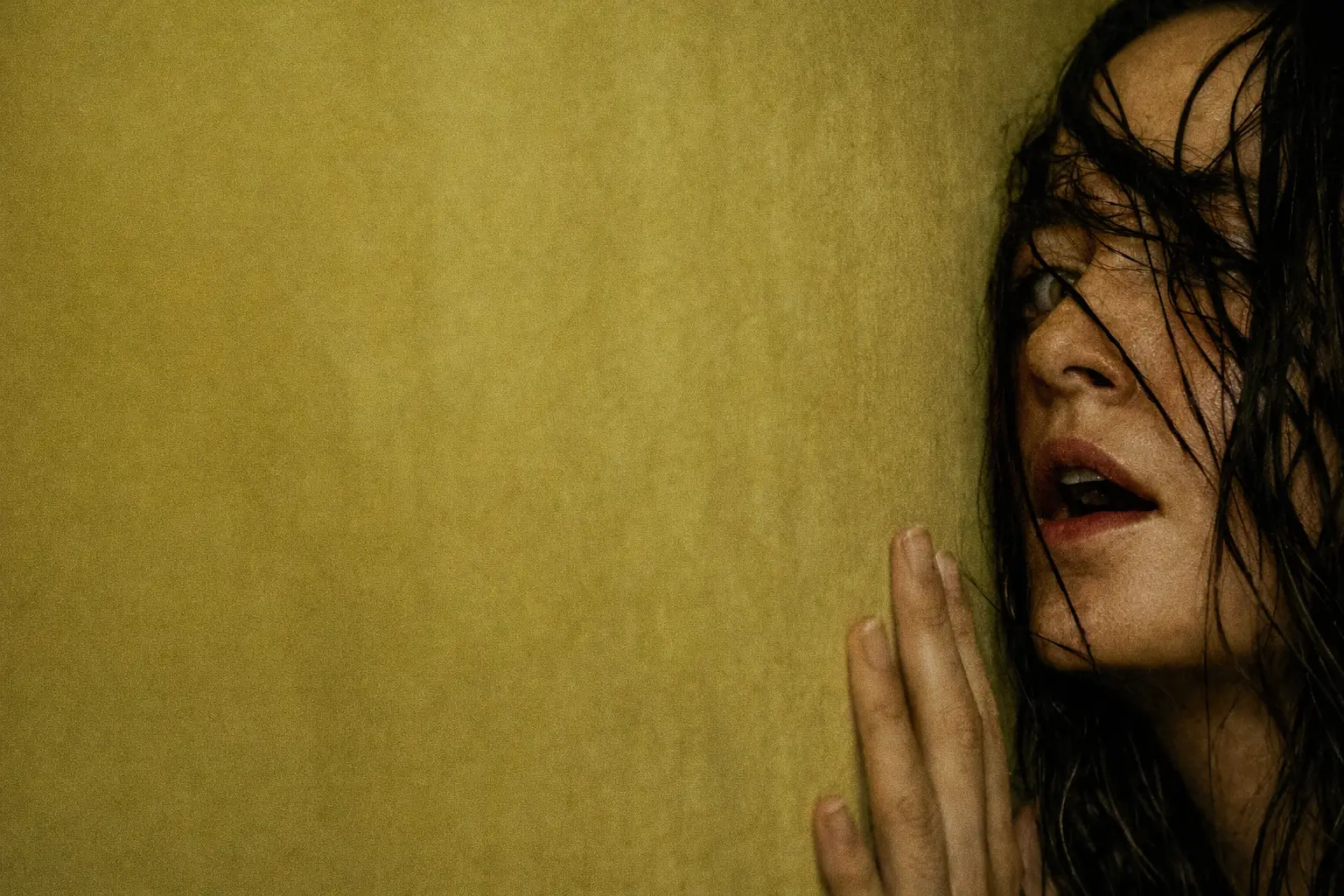 A distressed Renate Reinsve presses her hand against a yellow, fluorescent-lit wall, her damp hair partially obscuring her face as she looks upward with a tense, disoriented expression in a liminal interior setting