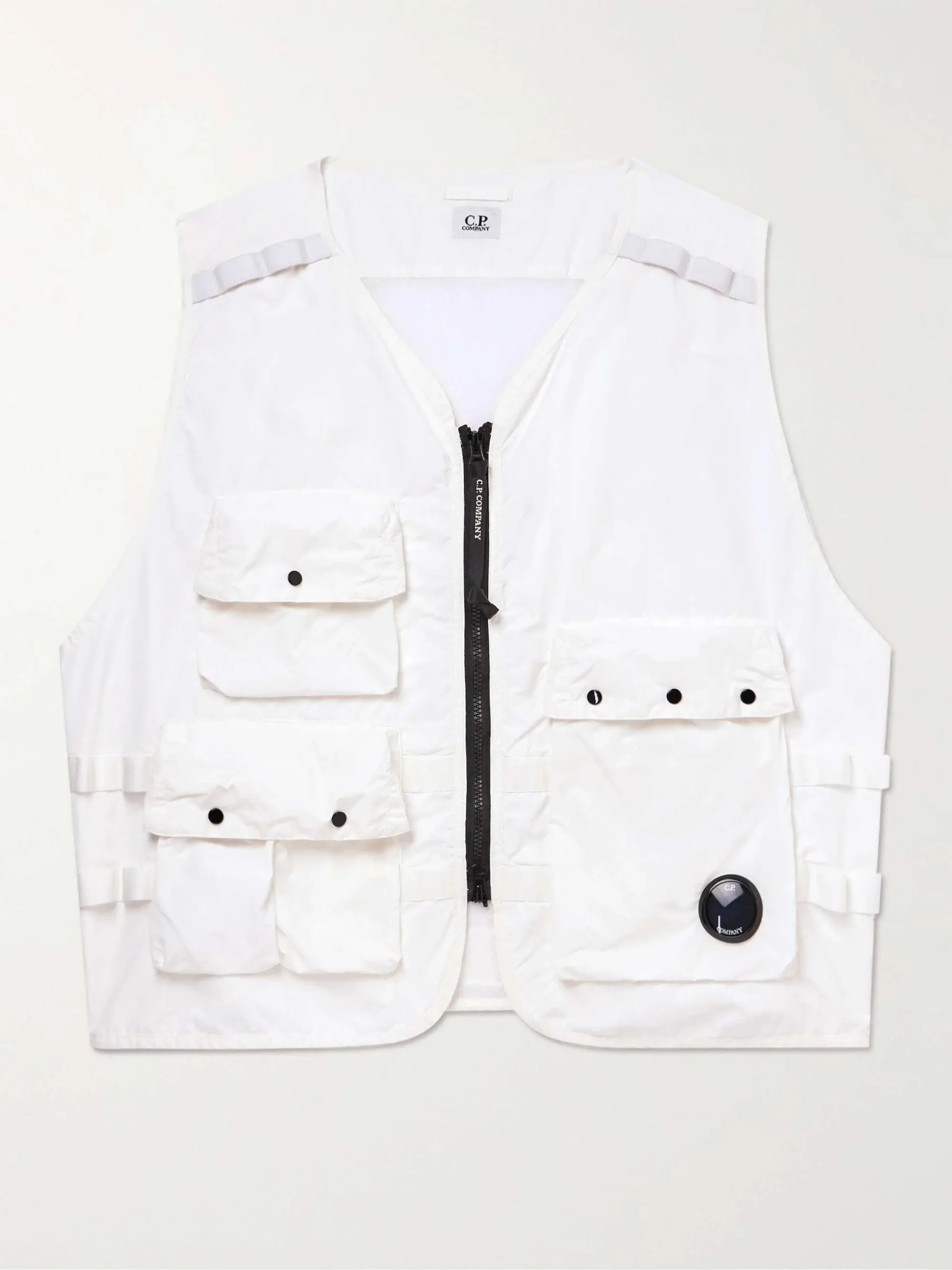 White C.P. Company utility vest featuring a lightweight technical shell, central zip closure, multiple flap cargo pockets with snap fastenings, adjustable side tabs, and signature lens detail at the hem in a functional, pocket-driven silhouette