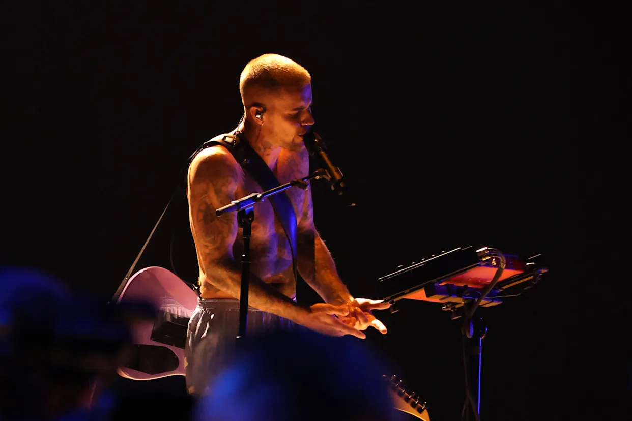 Justin Bieber mid-performance at a dimly lit venue, focused on vocals and keys with minimal stage production
