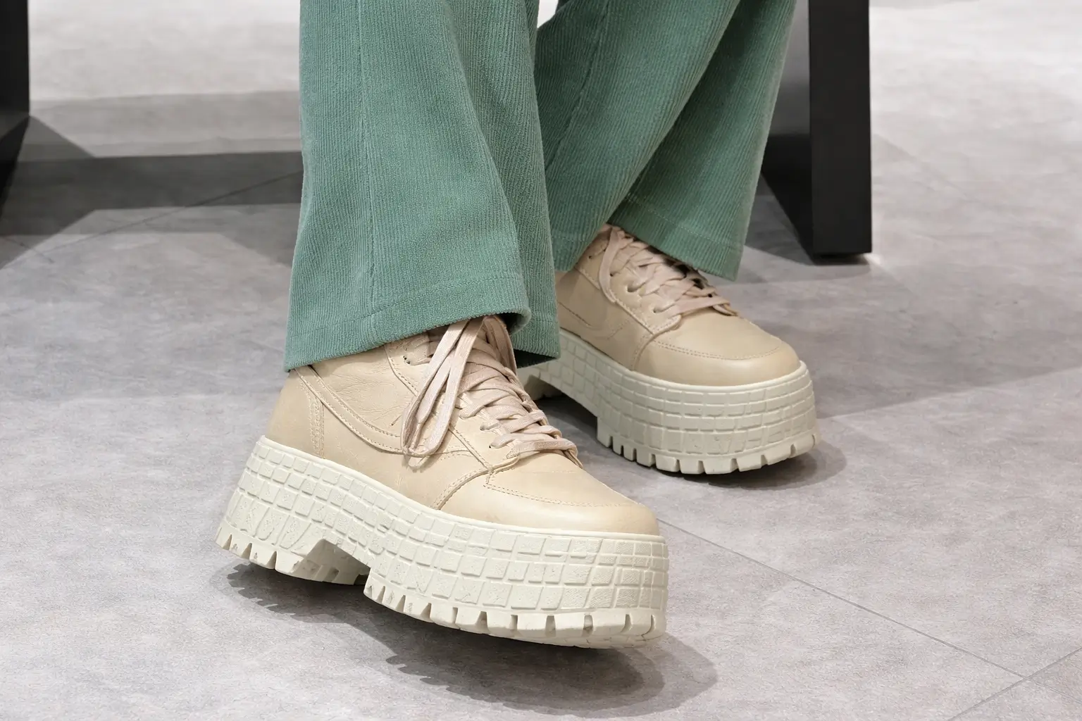 Glitched composite image of a person wearing a colorful striped sweater and chunky platform sneakers, with fragmented overlays, digital distortion bands, and misaligned layers obscuring the face and body against an outdoor setting with blue sky and pavement visible in the background