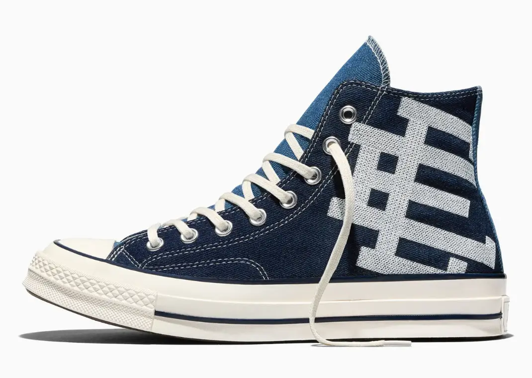 Eric Emanuel x Converse Chuck 70 high-top sneaker in indigo denim with contrast white stitching, cream laces, vintage off-white rubber sole, and oversized woven EE logo across the side panel