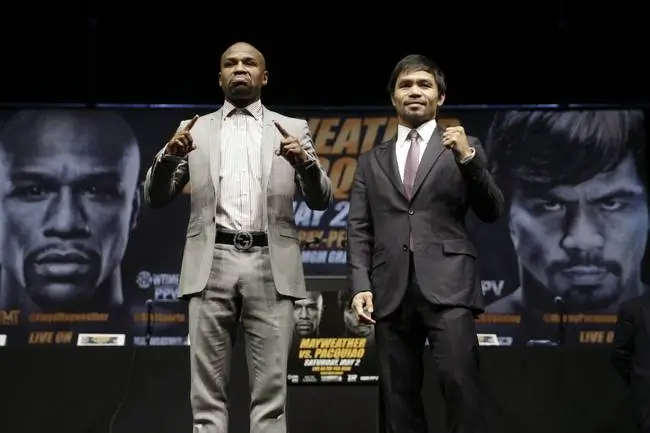 Floyd Mayweather Jr. and Manny Pacquiao pose during a press conference face-off, both raising their fists in front of promotional backdrops featuring their portraits, signaling anticipation for a high-profile rematch event