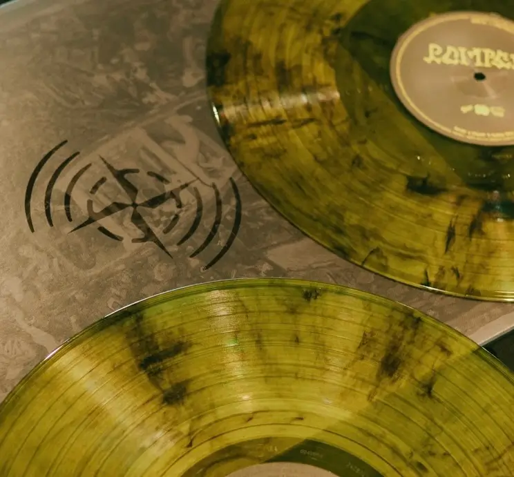 Close-up of marbled translucent vinyl records in yellow-green tones with black splatter detailing, placed on a textured sleeve featuring a Stone Island Sound-style graphic motif