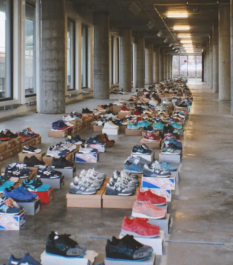 Wide interior shot of an industrial-style corridor lined with rows of sneaker boxes and pairs arranged in sequence, showcasing a large archival collection of various footwear models across concrete floors under natural window light