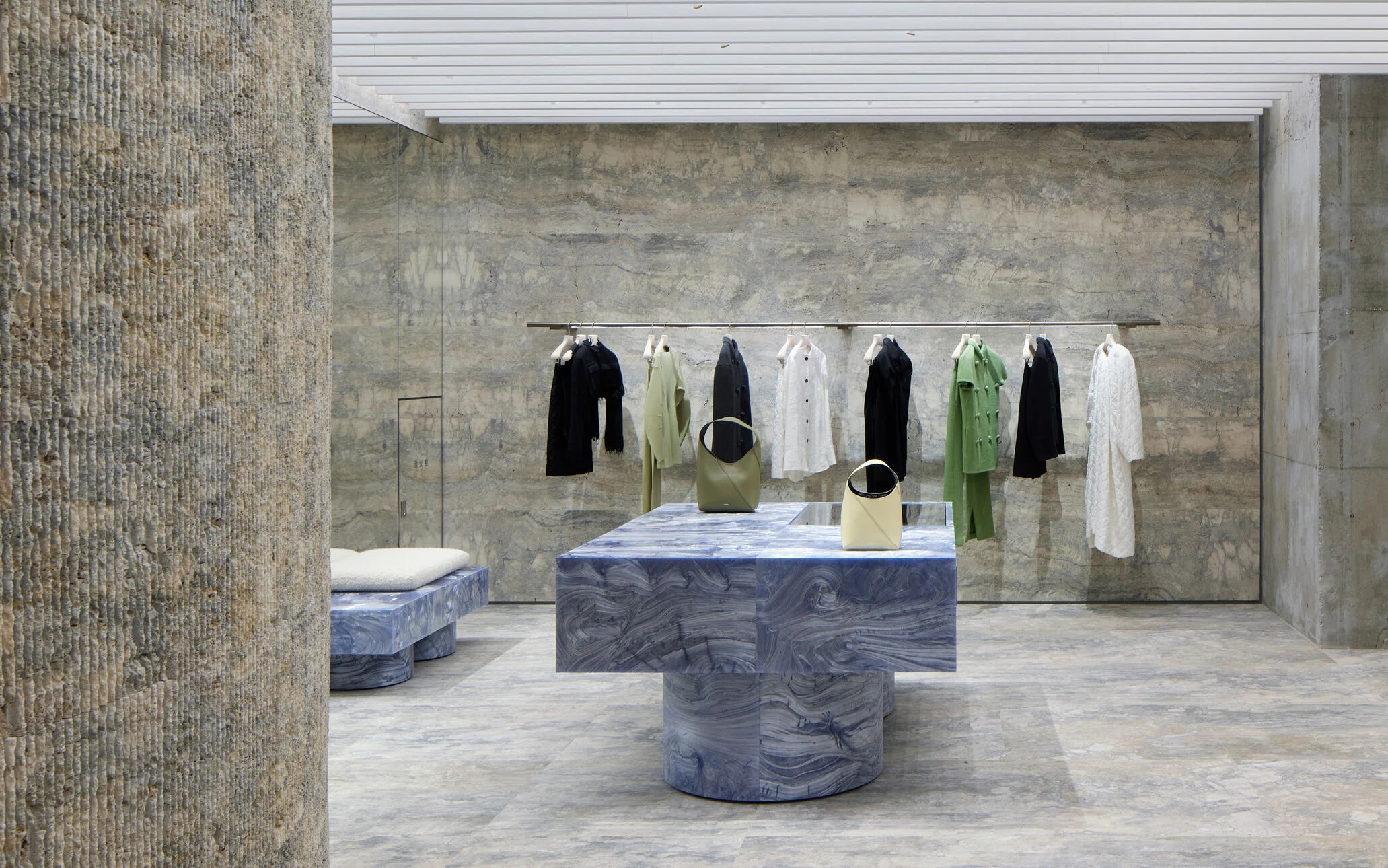 JIL SANDER Ginza flagship interior with minimalist stone walls, suspended garments, and sculptural blue marble display table