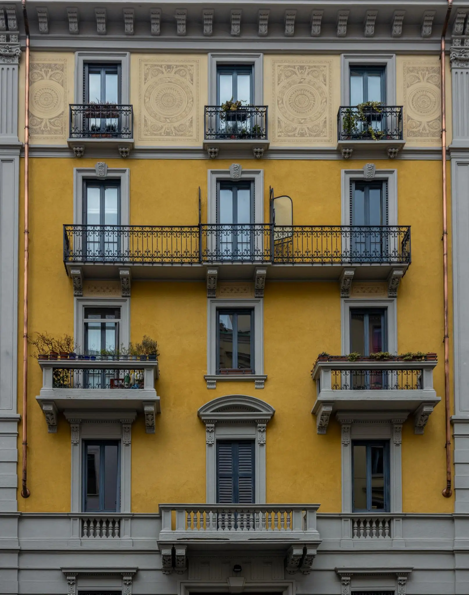 Yellow Milan apartment façade with ornate detailing, wrought-iron balconies, and symmetrical windows framed in gray stone
