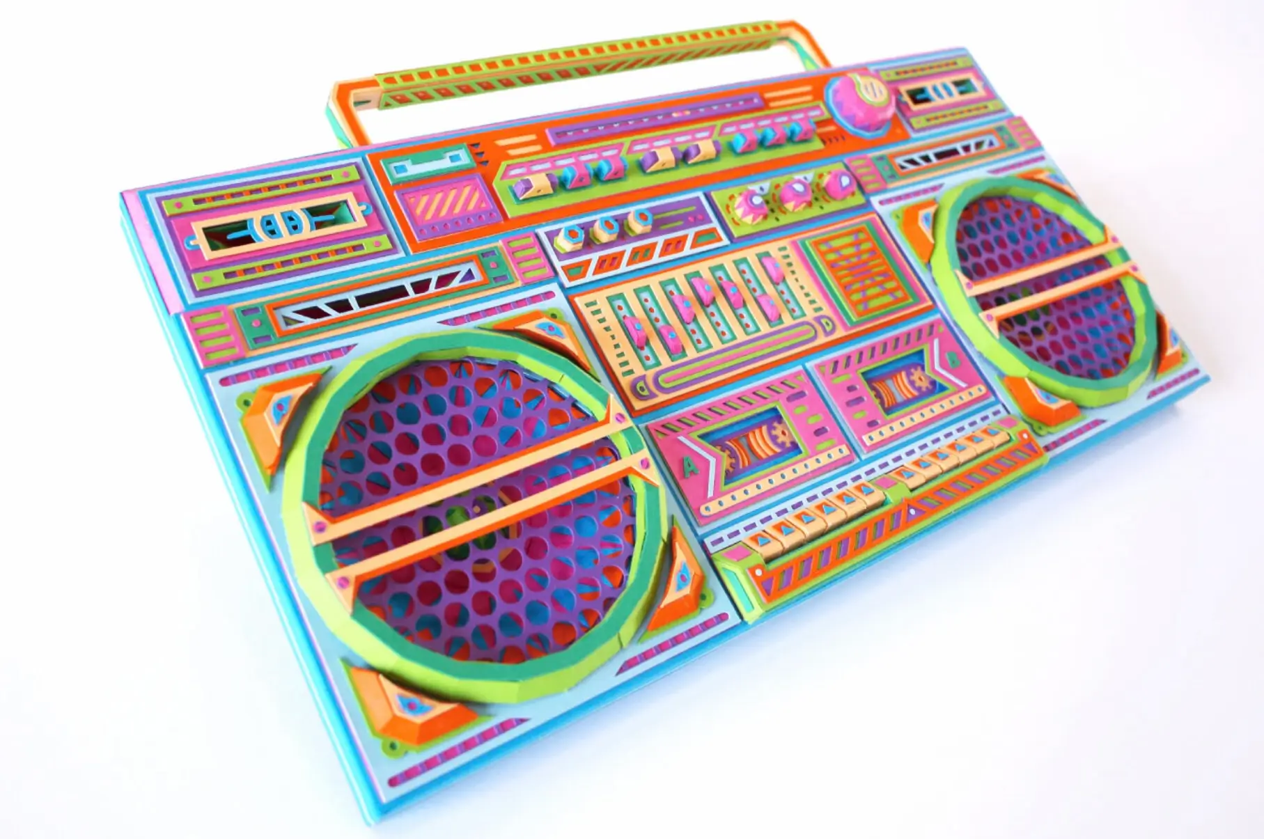 Angled view of a handmade paper boombox sculpture with layered speaker grilles, colorful geometric panels, and intricate cut-and-fold details, showcasing dimensional craftsmanship and vibrant retro-inspired design