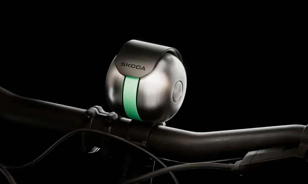 Close-up of Škoda Auto DuoBell mounted on a bicycle handlebar, featuring a brushed metal finish with a central green accent stripe against a black background