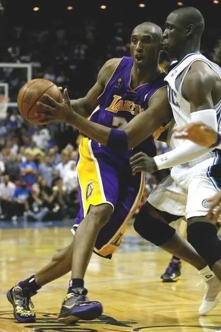 Kobe Bryant drives to the basket in a Los Angeles Lakers uniform, cradling the ball while being closely defended by an opposing Orlando Magic player during an in-game moment