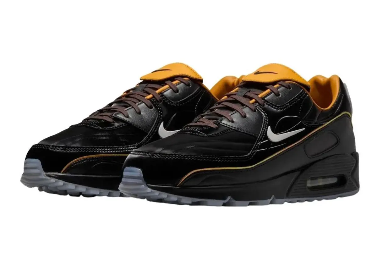 Nike Air Max 90 “Korea” pair in glossy black leather with brown laces, golden-orange tongue and piping accents, white Swoosh branding, and visible Air cushioning over a semi-translucent outsole