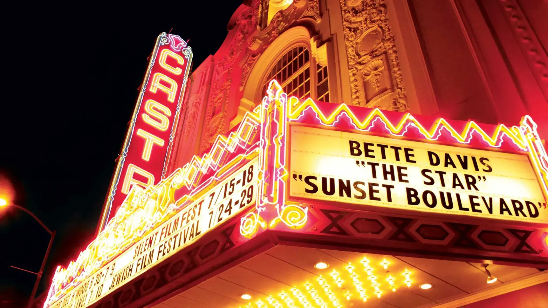 Neon-lit marquee of the Castro Theatre glows against the night sky, its ornate façade framing classic film titles and festival signage in vivid red and gold illumination