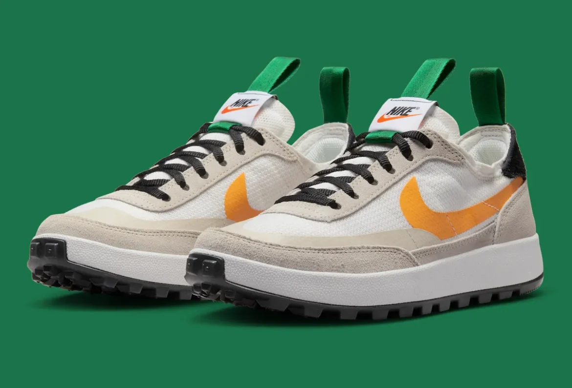 Pair of Tom Sachs x Nike NikeCraft General Purpose Shoe “Bricolage” sneakers in Summit White, shown at a three-quarter angle with beige suede overlays, bold University Gold Swooshes, black laces, green pull tabs, and rugged black lug outsoles against a green backdrop