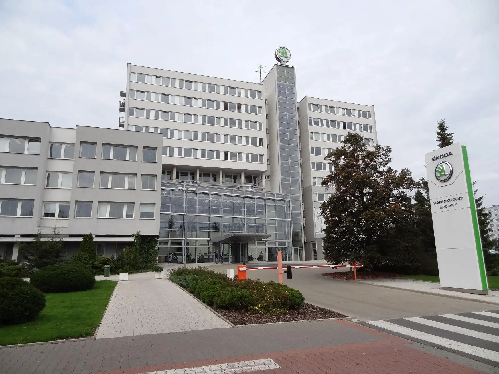 Exterior view of Škoda Auto headquarters building with glass entrance façade, modern office structure, and branded sign in front under overcast sky