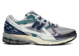 New Balance 1906U sneaker in white and silver mesh with teal and navy accents, featuring layered overlays, ABZORB cushioned sole, and classic lace-up design
