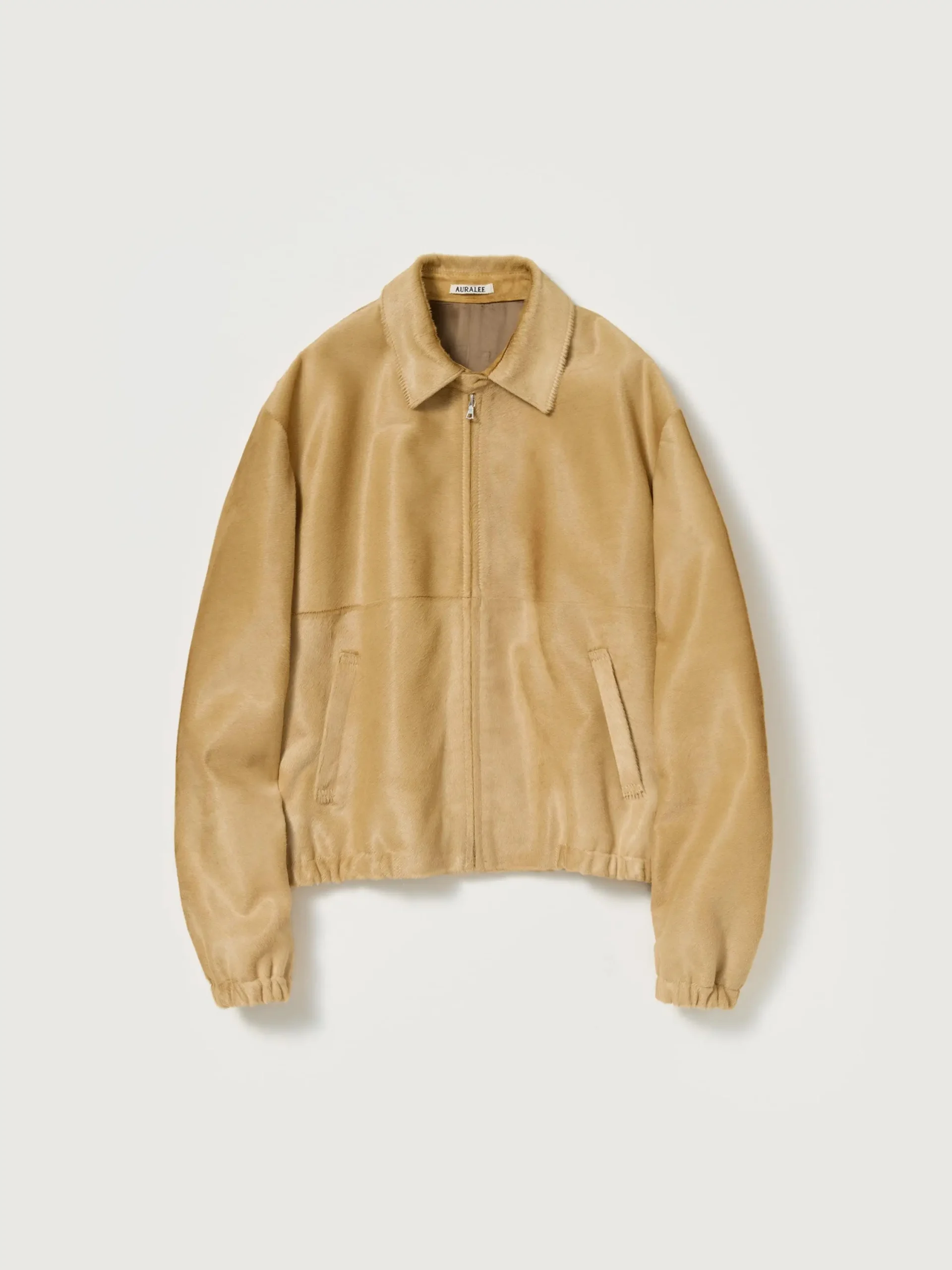 Camel-toned calf hair zip blouson by Auralee featuring a soft textured surface, clean front zip closure, subtle welt pockets, and gently elasticated hem and cuffs in a minimalist silhouette